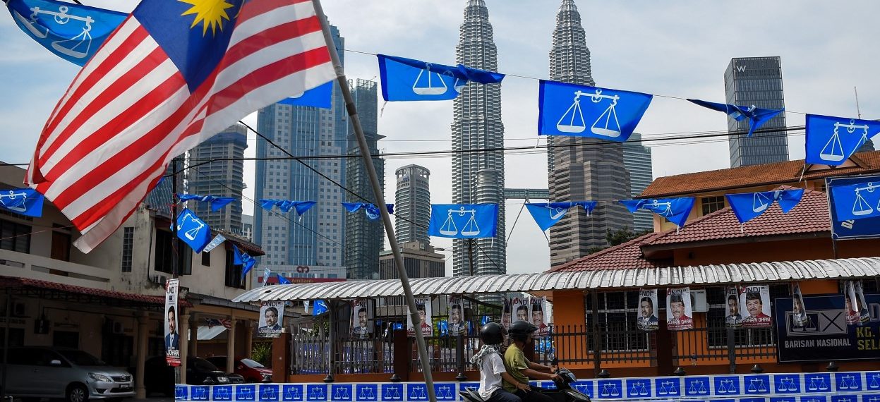 Malaysia’s Petronas Twin Towers in Kuala Lumpur loom in the background as a motorist rides past the ruling coalition party Barisan Nasional’s flags on the eve of the last general election (GE14), which was held on 9 May 2018. (Photo: Manan VATSYAYANA/ AFP)