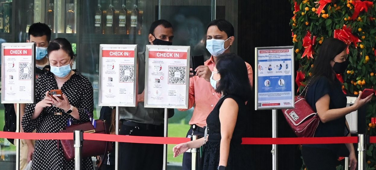 People scan QR codes using the Trace Together contact tracing app on their smartphones before entering a building at the Raffles Place financial business district in Singapore on 14 February 2022. (Photo: Roslan RAHMAN/ AFP)