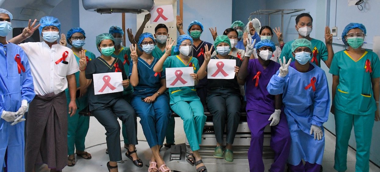 Medical staff make a three finger salute with red ribbons on their uniforms inside a hospital in Yangon on 3 February, 2021 as calls for a civil disobedience gather pace following a military coup detaining civilian leader Aung San Suu Kyi. (Photo: STR/ AFP)