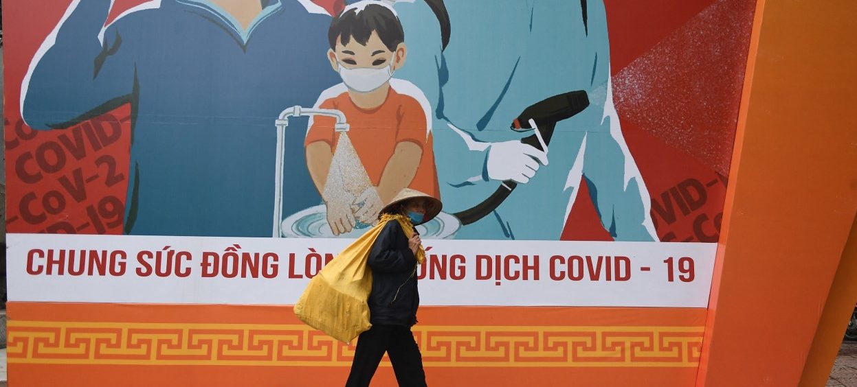 A woman walks past a billboard with information on preventing the spread of the Covid-19 coronavirus in Hanoi, taken on 19 October 2021. (Photo: Nhac NGUYEN/ AFP)