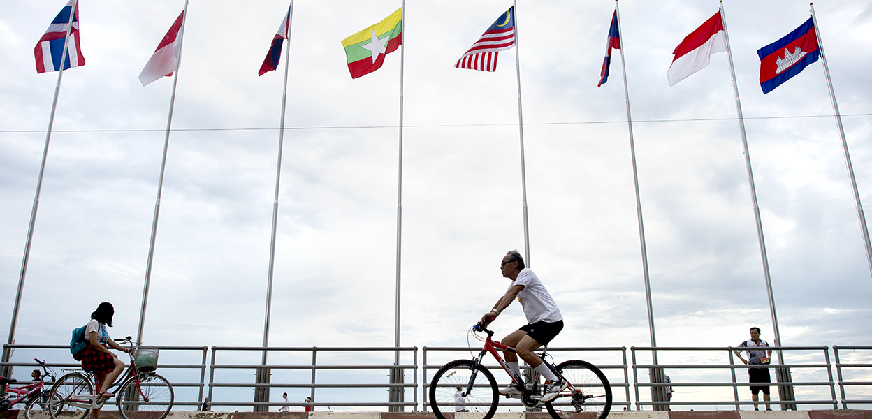People pass by flags of ASEAN countries along the banks of the Mekong River in Vientiane