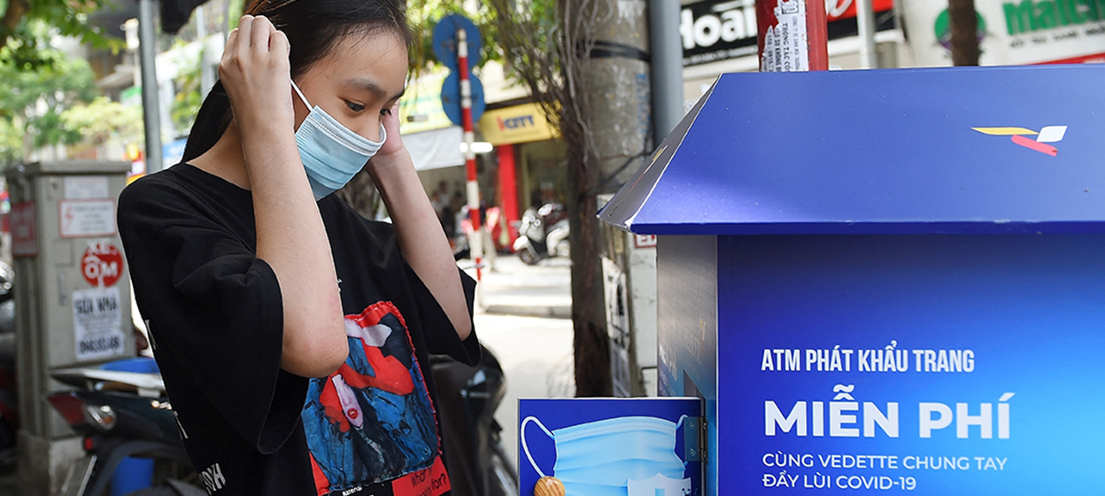 A girl wears a face mask from a "free mask" dispenser