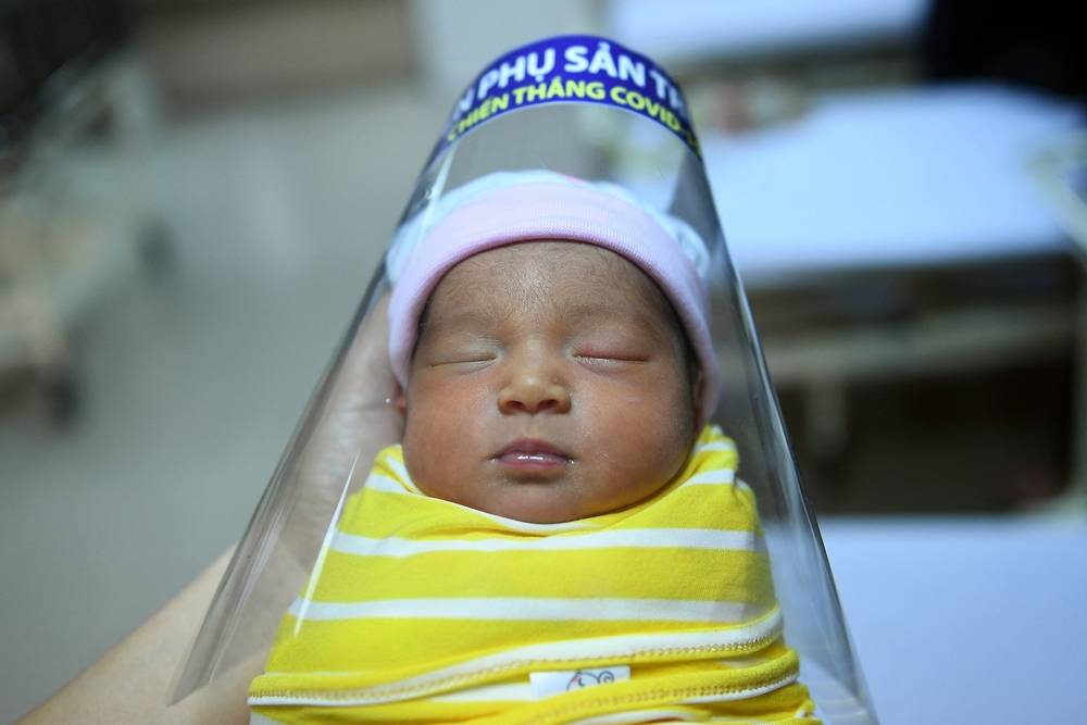 A nurse holds a newborn baby wearing a face shield
