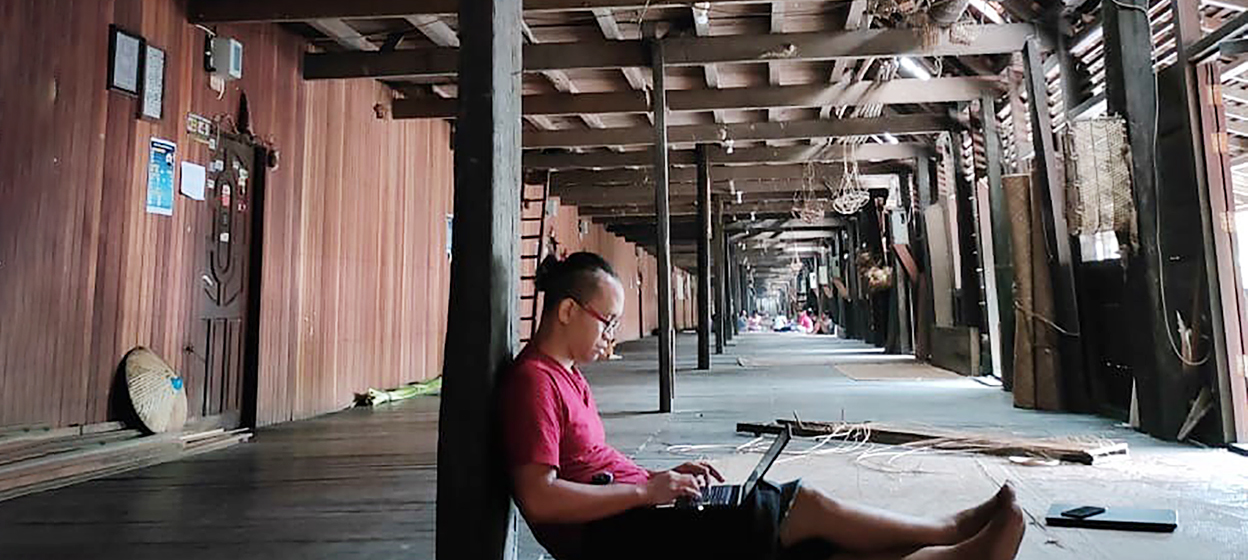 A man on his laptop at a longhouse in Sungai Utik